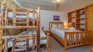 Ein Zimmer mit zwei Etagenbetten, einem hölzernen Kopfteil, einem Nachttisch, einer Lampe und einem gerahmten Bild an der Wand.