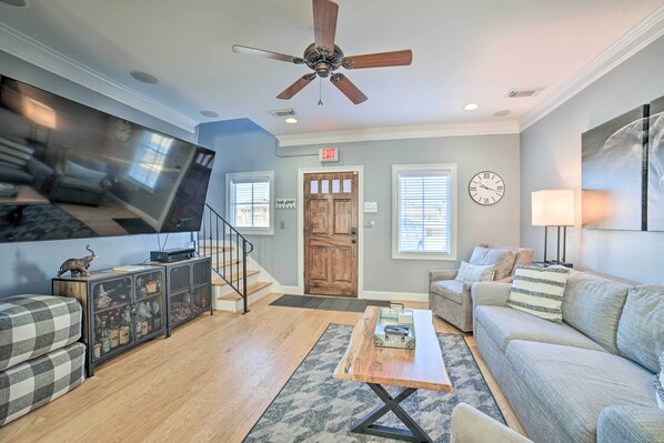 A living room with a sofa, a coffee table, a TV, a cabinet, and a ceiling fan. - Modern Retreat ~ 1/2 Mi to Bryant-Denny Stadium (Tuscaloosa)