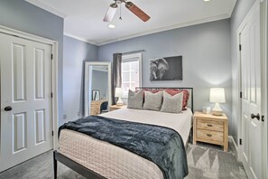A bedroom with a bed, nightstands, a ceiling fan, a window with curtains, and a wall-mounted artwork. - Modern Retreat ~ 1/2 Mi to Bryant-Denny Stadium (Tuscaloosa)