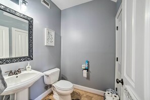 A bathroom with a white sink, toilet, and mirror. There is a framed picture on the wall and a roll of toilet paper dispenser. - Modern Retreat ~ 1/2 Mi to Bryant-Denny Stadium (Tuscaloosa)