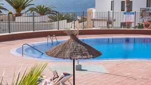 Un espace piscine avec vue sur la mer, un parasol en chaume et une bouée de sauvetage.