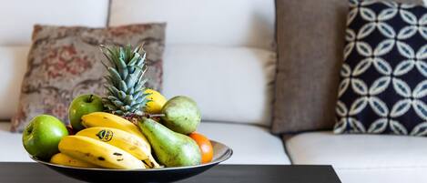 A fruit bowl on a table in front of a white sofa with patterned cushions.