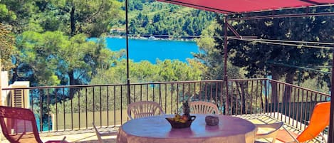 A balcony with a table and chairs, overlooking a lake and forested area.