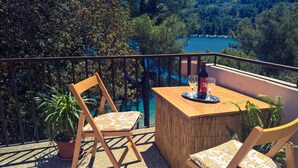 A balcony with two wooden chairs, a small table, and a bottle of wine. - Seafront Apartment Dana (Vela Luka)