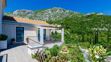 Ein modernes Haus mit Ziegeldach, einem Balkon mit Metallgeländer und Blick auf grüne Hügel und Berge im Hintergrund.