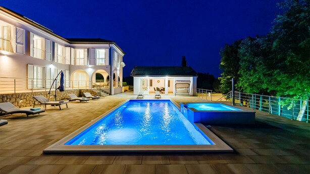 Ein zweistöckiges Haus mit Swimmingpool und Liegestühlen.