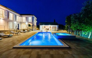 Ett tvåvåningshus med en swimmingpool och solstolar.
