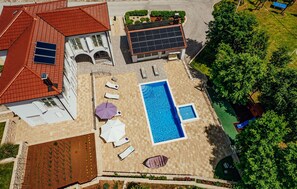 En vy från ovan av en fastighet med en swimmingpool, solstolar, en täckt uteplats och en uppsättning solpaneler.