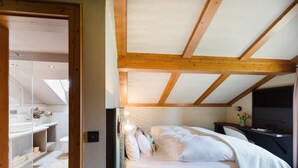 A bedroom with a wooden ceiling, a bed with white bedding, a bedside table, and a TV. - Double Deluxe - Landhaus Christl am See (Bad Wiessee)