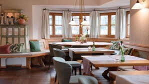 A cozy dining area with wooden tables and chairs, a bench, and a cabinet with decorative items. - Double Deluxe - Landhaus Christl am See (Bad Wiessee)