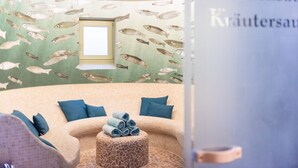 A spa room with a curved sofa, blue pillows, a round ottoman with towels, and a wall mural of fish. - Double Deluxe - Landhaus Christl am See (Bad Wiessee)
