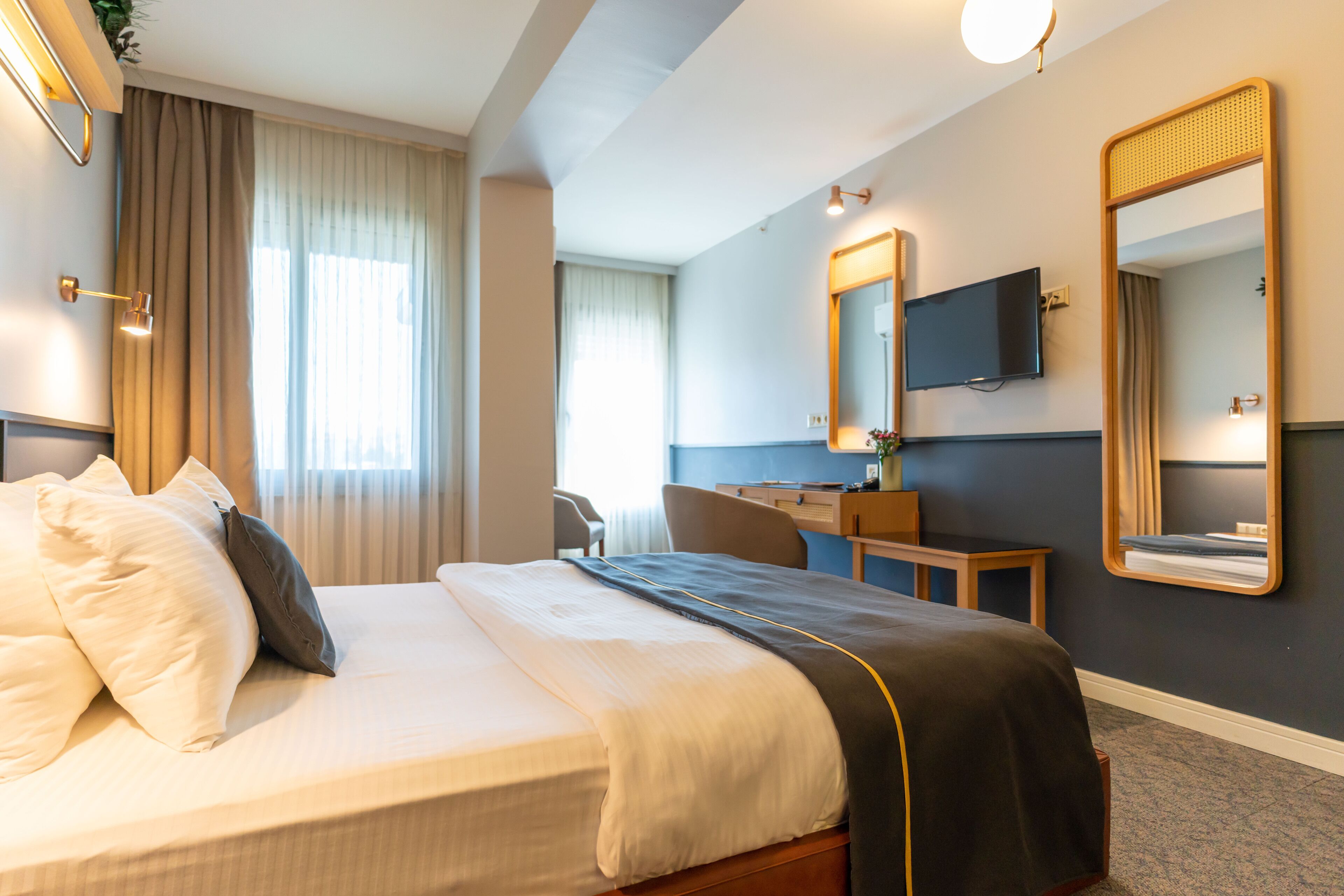 A hotel room with a bed, a desk, a chair, a TV, and a large mirror.
