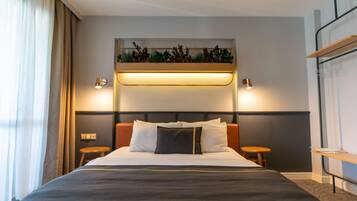 Una habitación de hotel moderna con una cama grande, mesitas de noche, un estante en la pared con plantas y una lámpara en el techo.