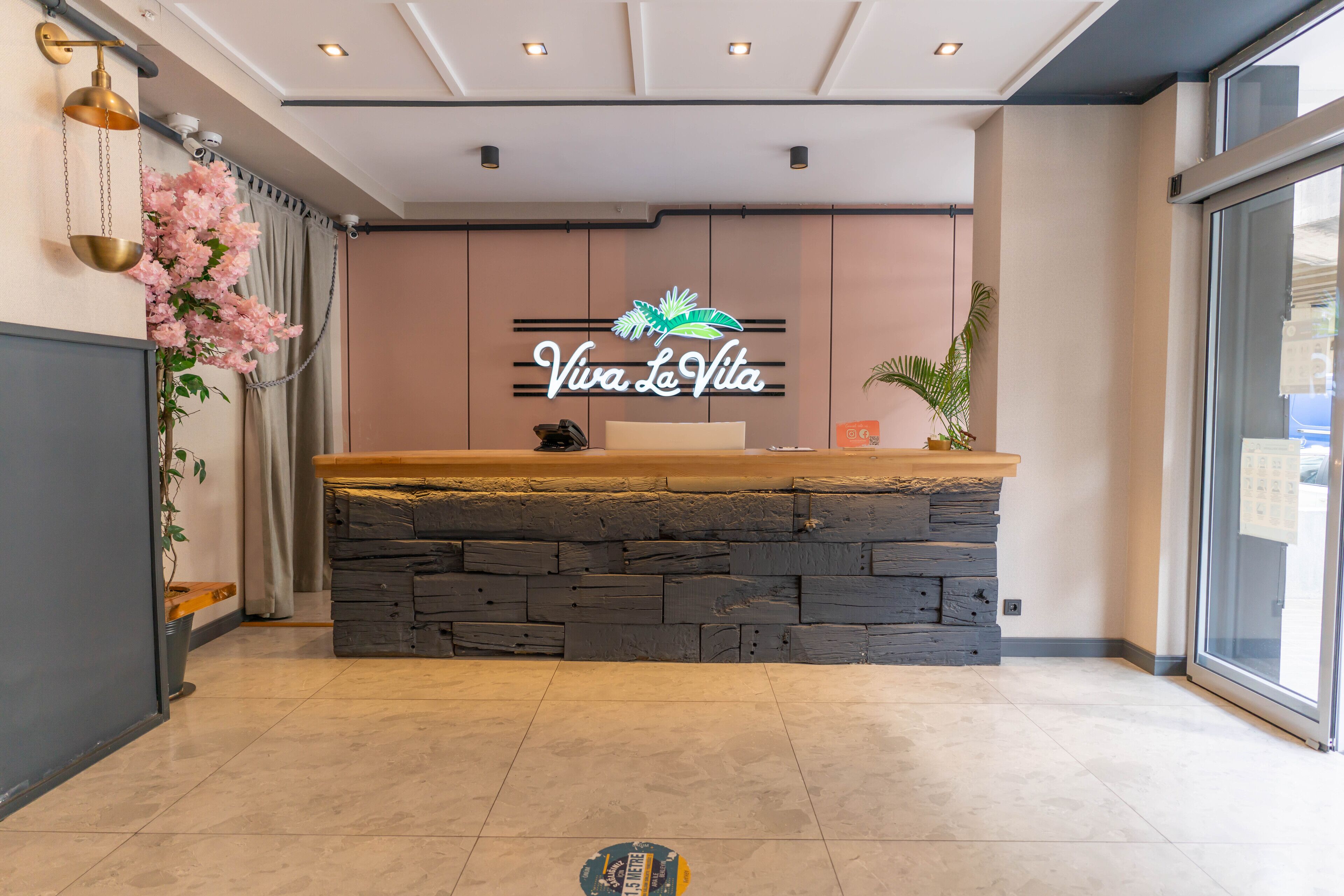 A reception area with a stone counter, a neon sign reading "Viva La Vita," and a large window.