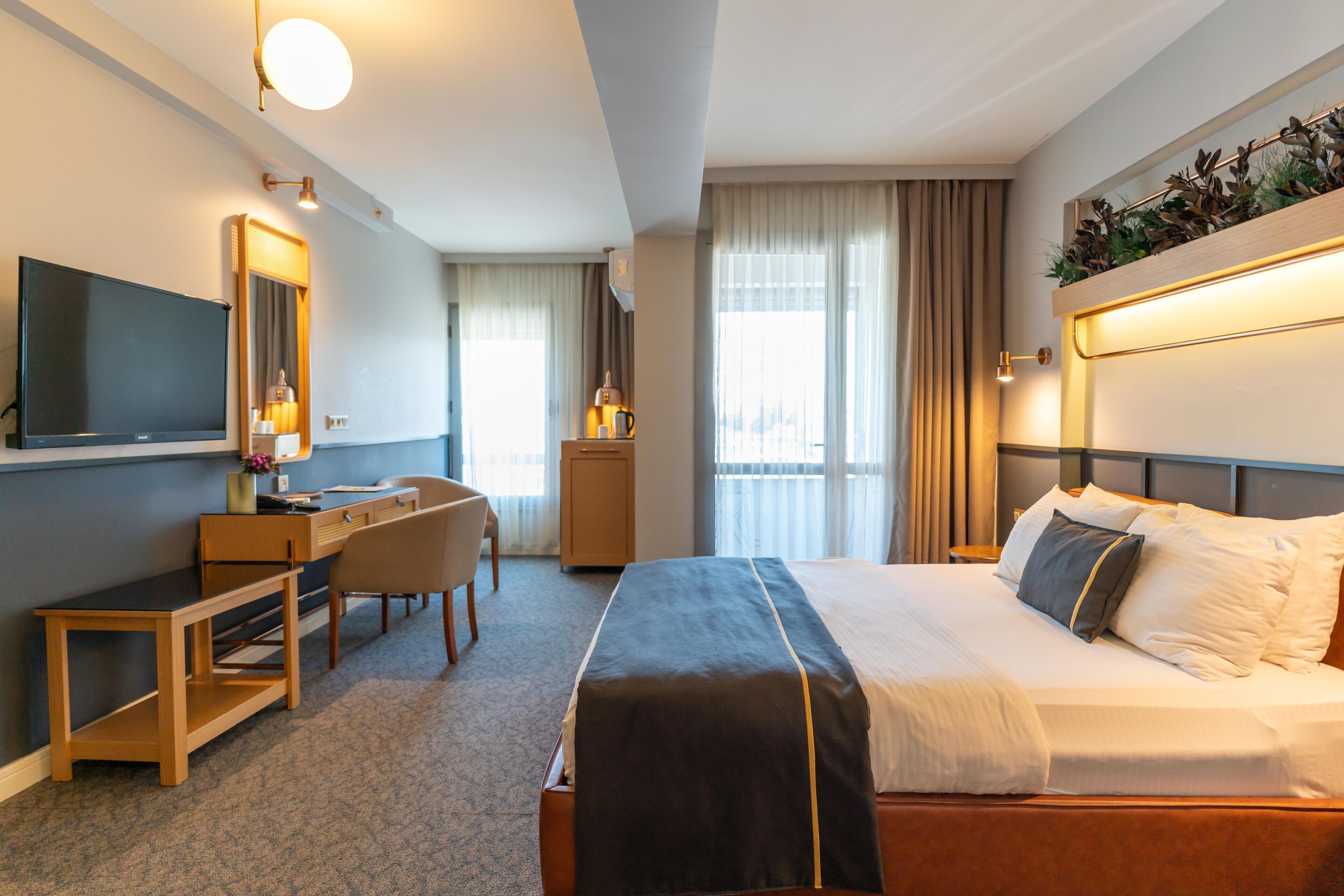 A hotel room with a bed, a desk, a chair, a TV, and a large window with curtains.