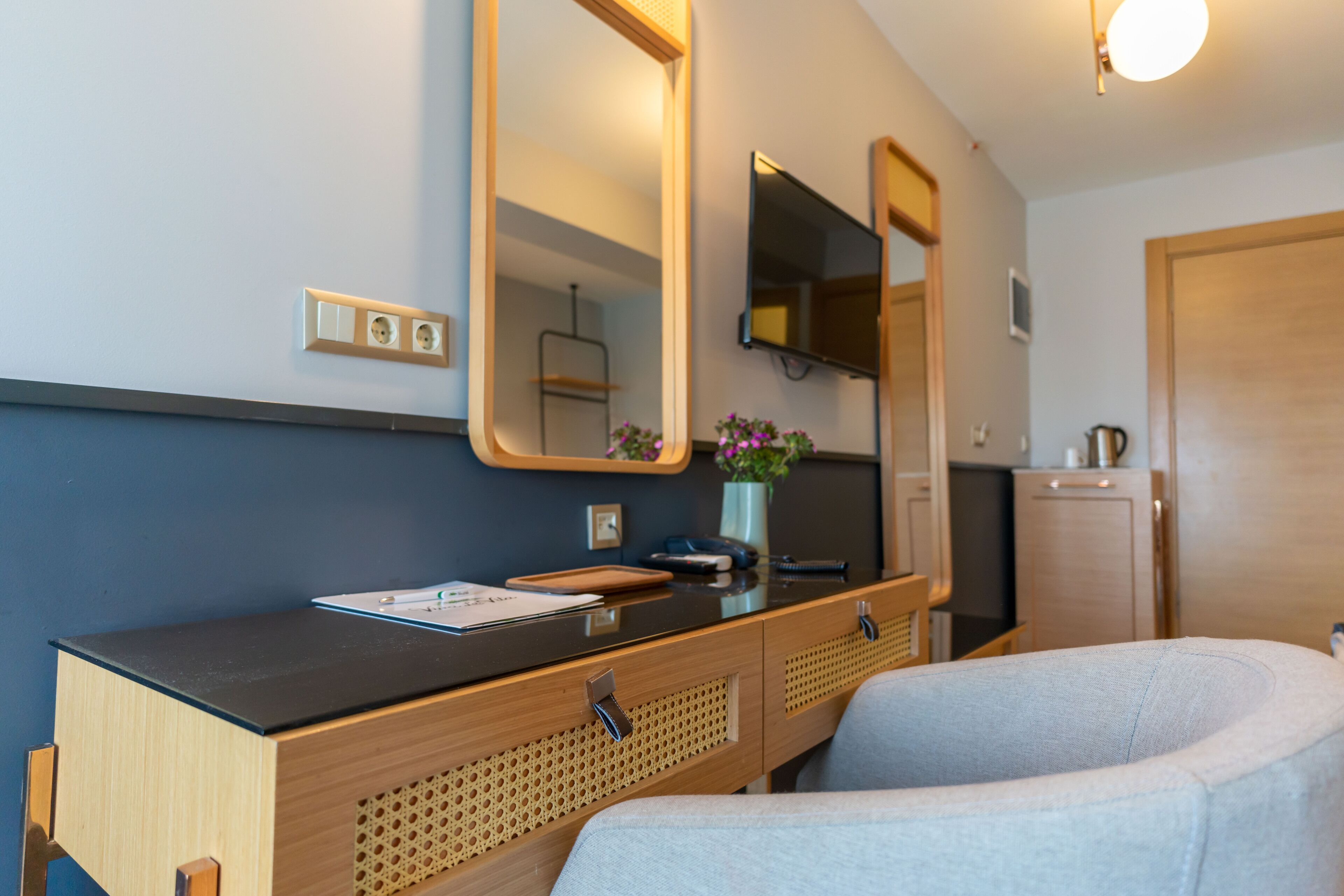 Una habitación compacta con tocador de madera, espejo, escritorio pequeño y zona de estar con cojines.