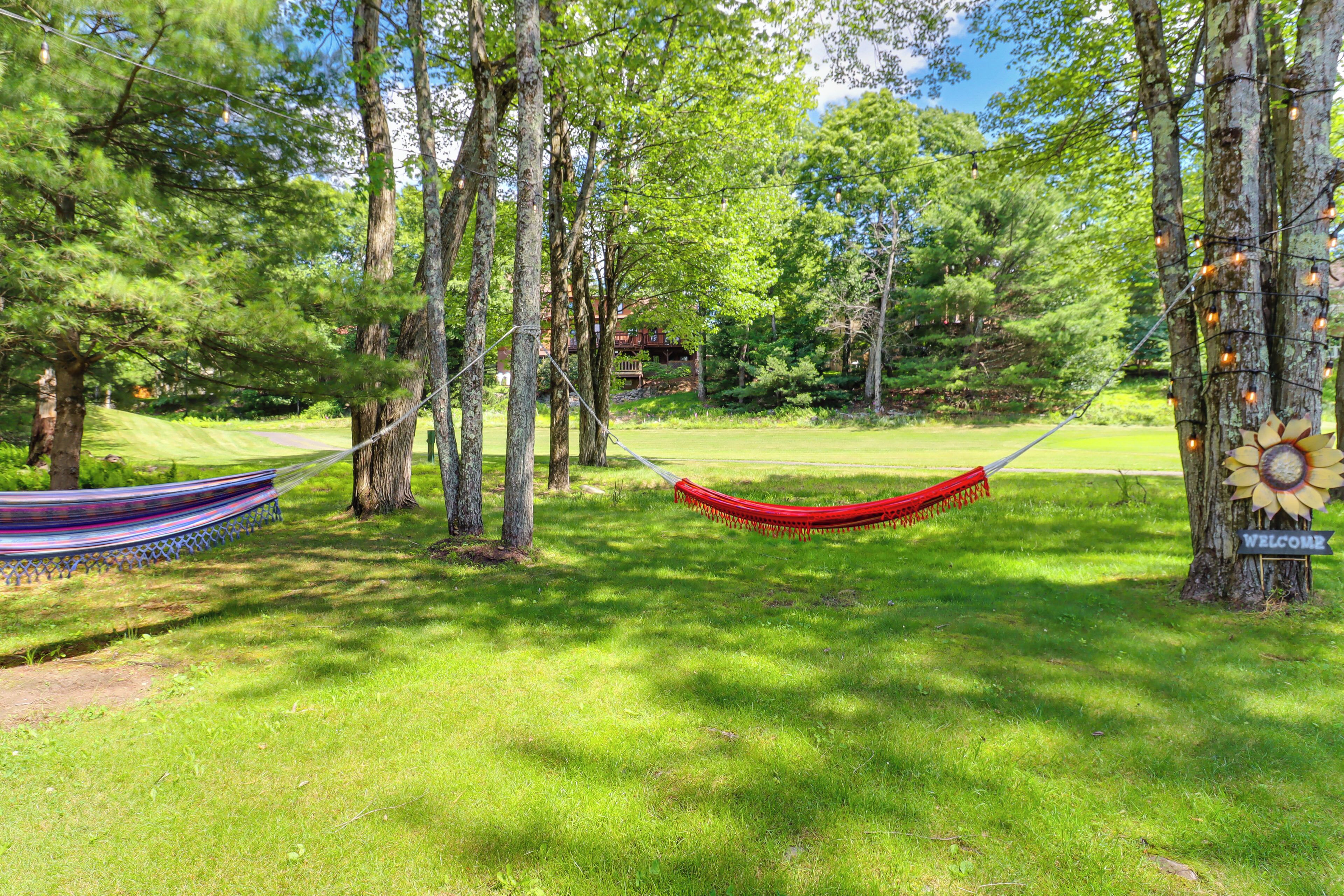 A hammock between trees in a grassy area with a 'WELCOME' sign on a tree.
