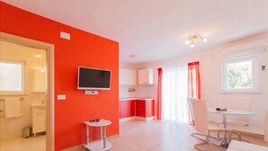 Um apartamento moderno com uma parede de destaque vermelha, cozinha com armários vermelhos, área de jantar com mesa de vidro e sala de estar com TV de tela plana.