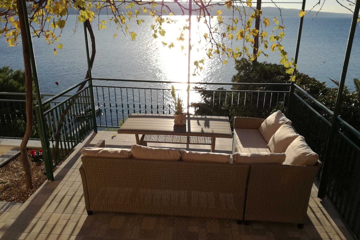 A balcony with wicker furniture, a table, and a view of the sea.