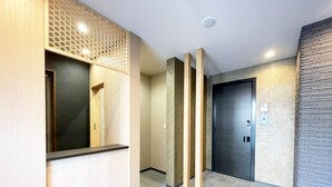 A modern hallway with a reception desk, a door with a keypad, and a textured wall. - HOTEL CLA-SS HIROSHIMA - Dobashi (Hiroshima)