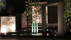 A modern two-story building with a balcony on the upper floor, a gated entrance, and a small garden area with a tree and decorative lights. - HOTEL CLA-SS HIROSHIMA - Dobashi (Hiroshima)