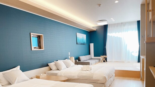 A hotel room with two beds, a sofa, a small table, and a large window with curtains. - HOTEL CLA-SS HIROSHIMA - Dobashi (Hiroshima)
