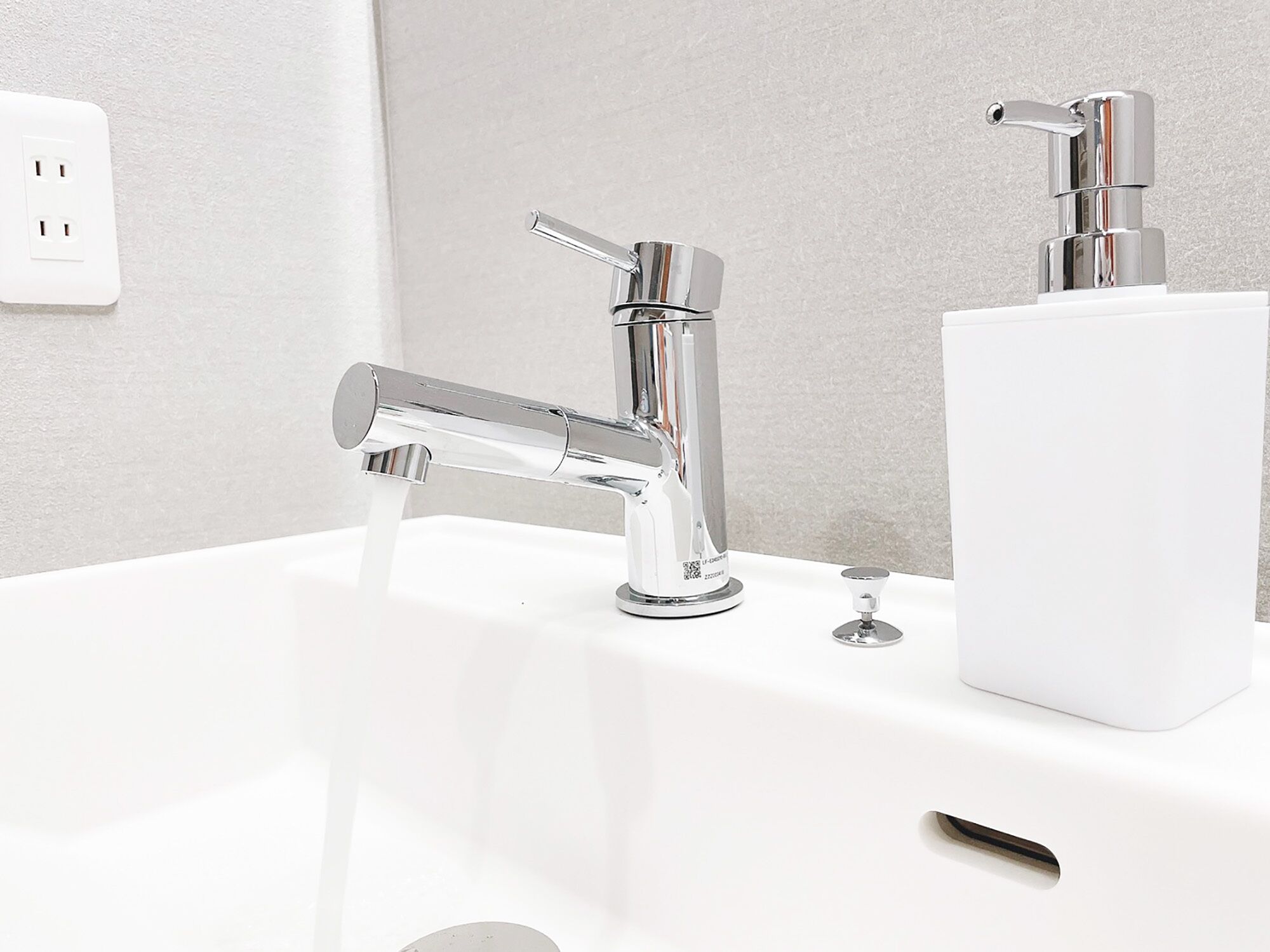 Een moderne badkamer met een chromen kraan, een zeepdispenser en een stopcontact op de muur.