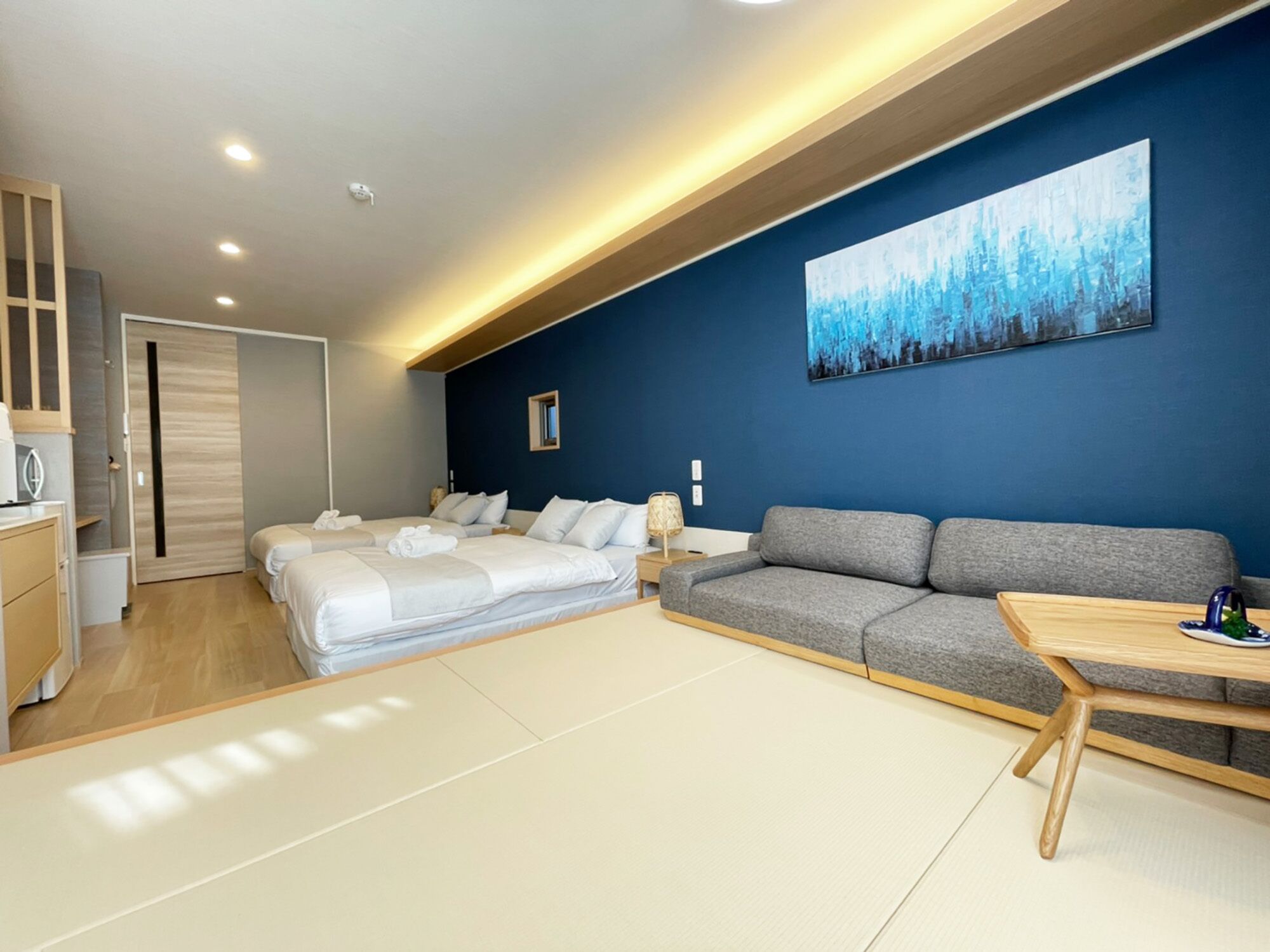 Una habitación de hotel moderna con una cama grande, un sofá, una mesita y un cuadro en la pared.