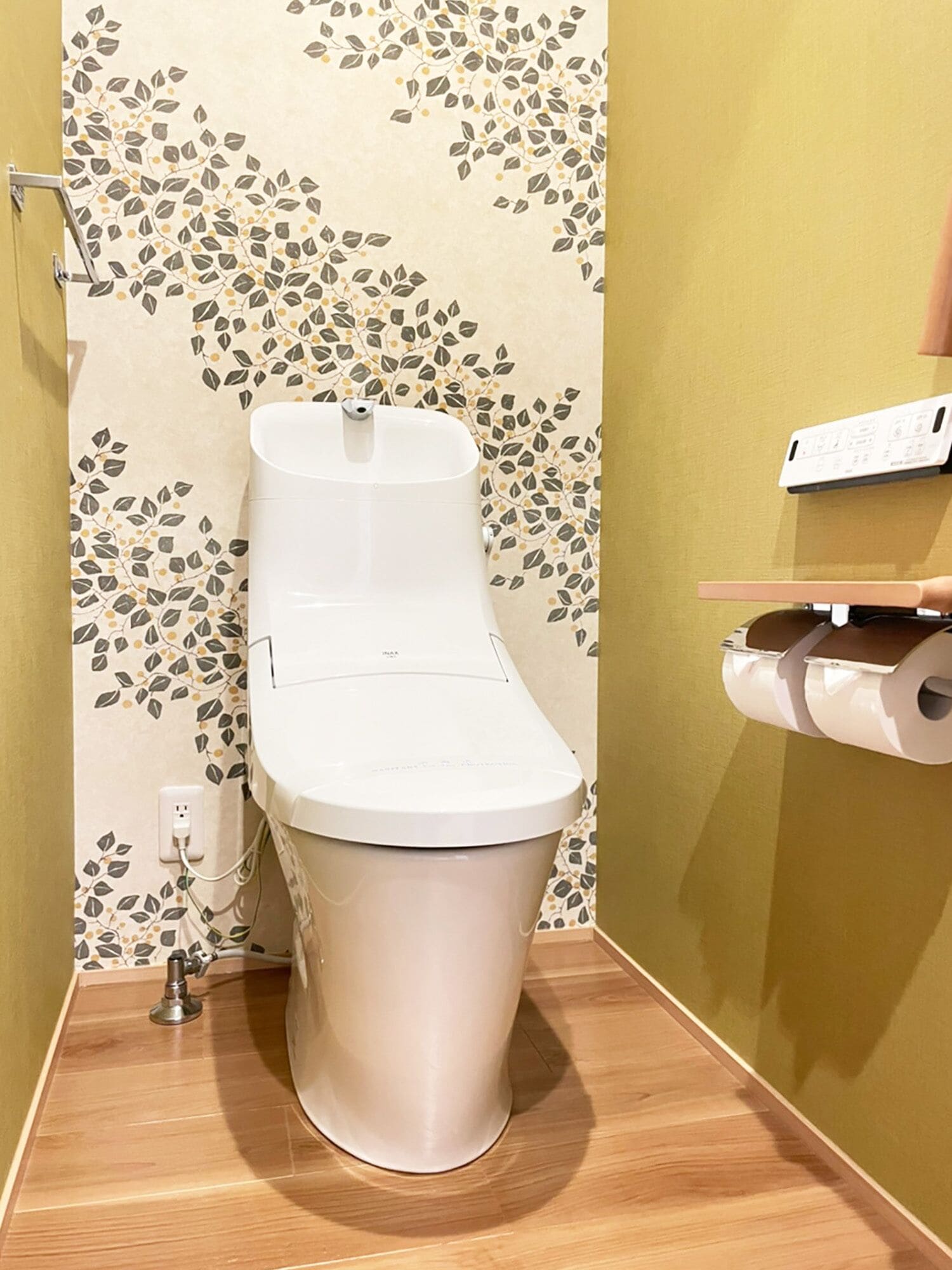 A toilet in a bathroom with a floral wallpaper pattern and a wooden floor.