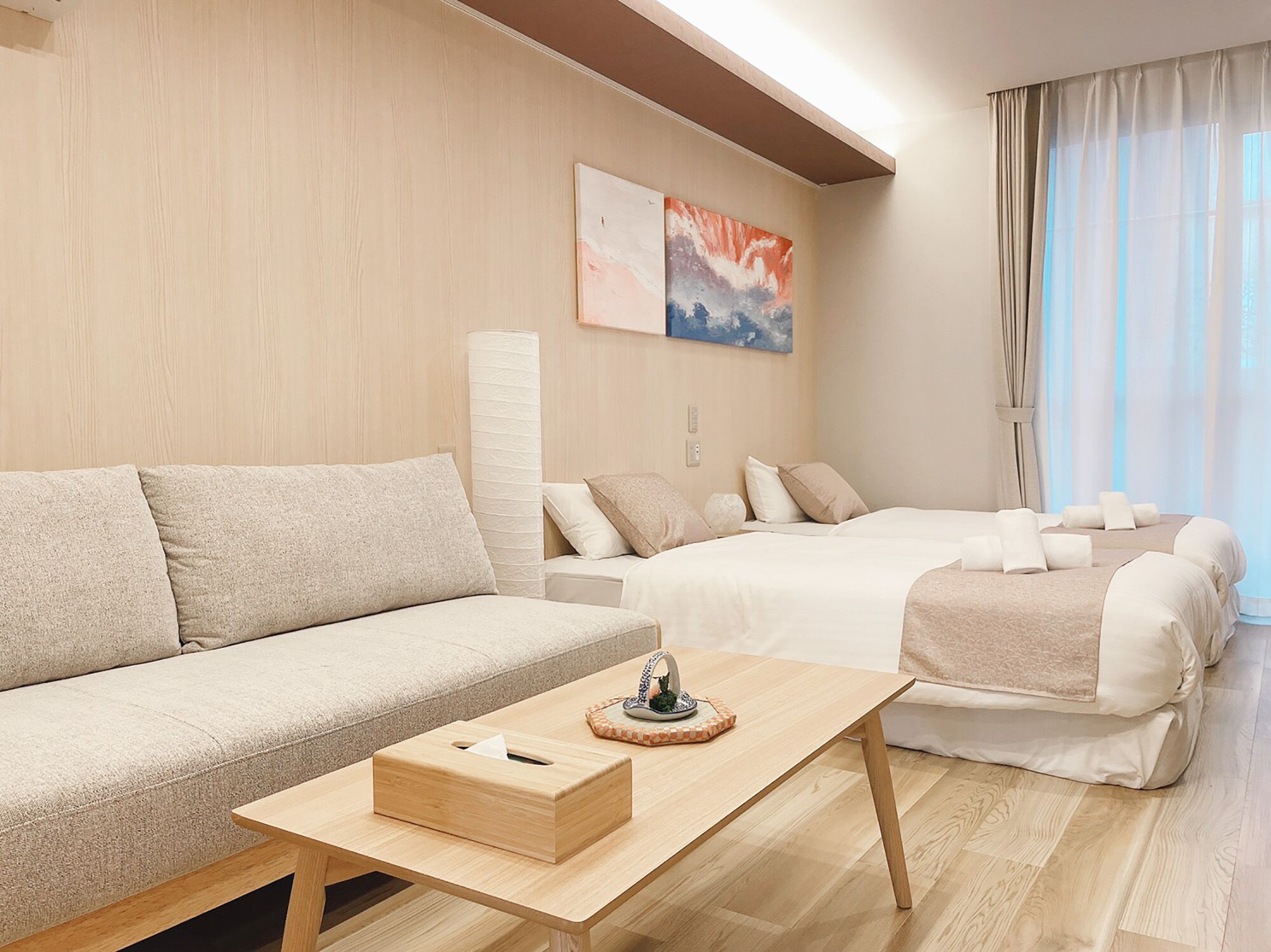 Una habitación de hotel moderna con sofá, cama, mesita de madera y un amplio ventanal con cortinas.
