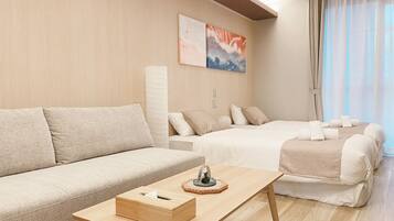 Una habitación de hotel moderna con sofá, cama, mesita de madera y un amplio ventanal con cortinas.