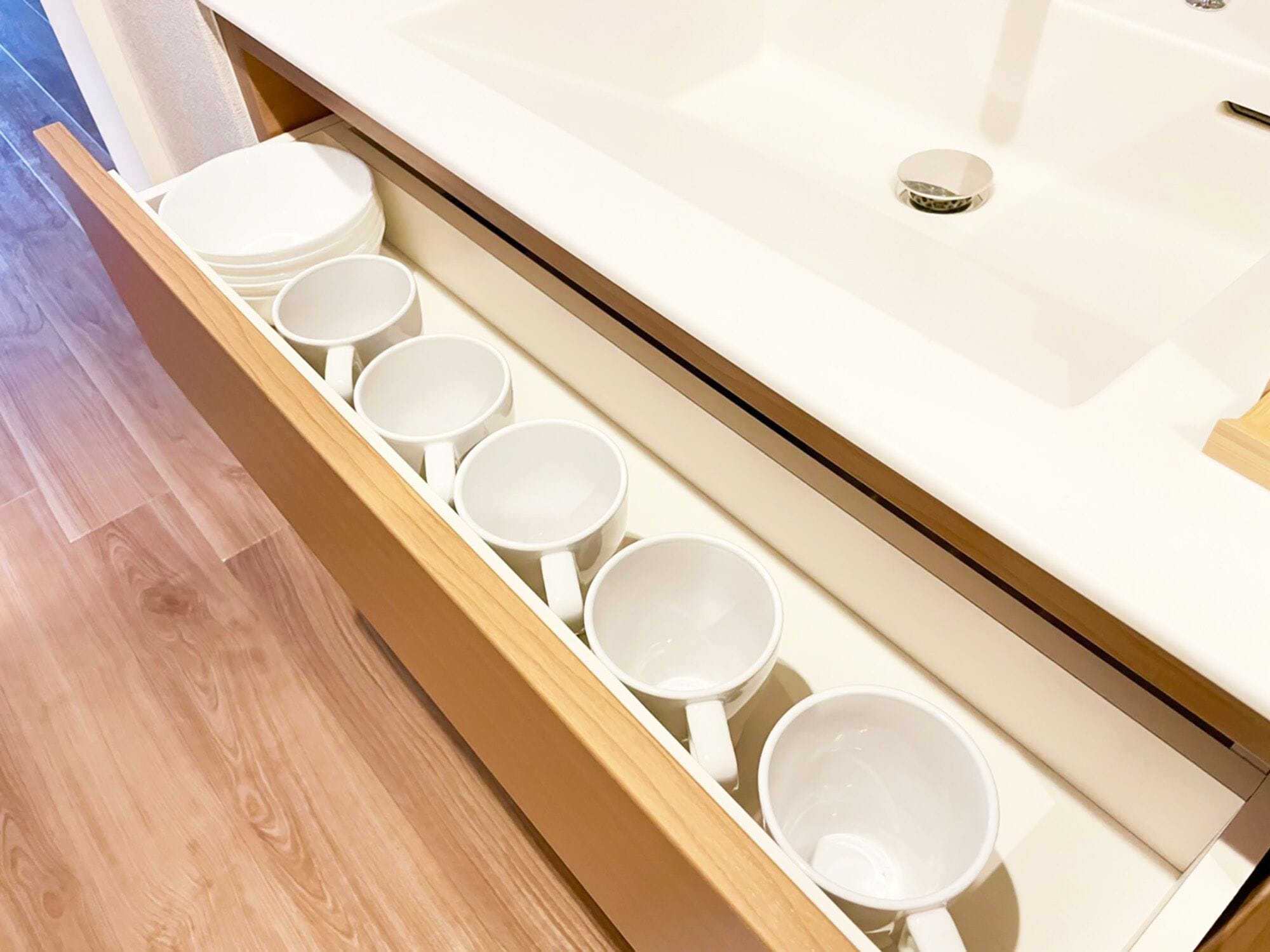A bathroom with a wooden floor, a white sink, and a drawer containing white mugs.