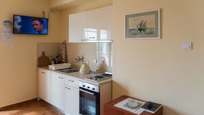 Una cocina compacta con armarios blancos, una estufa y un lavabo. Hay un cuadro en la pared y un televisor montado sobre la encimera.
