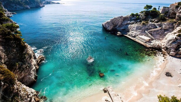 Un paisaje costero con aguas turquesas cristalinas, acantilados rocosos y una playa de arena.