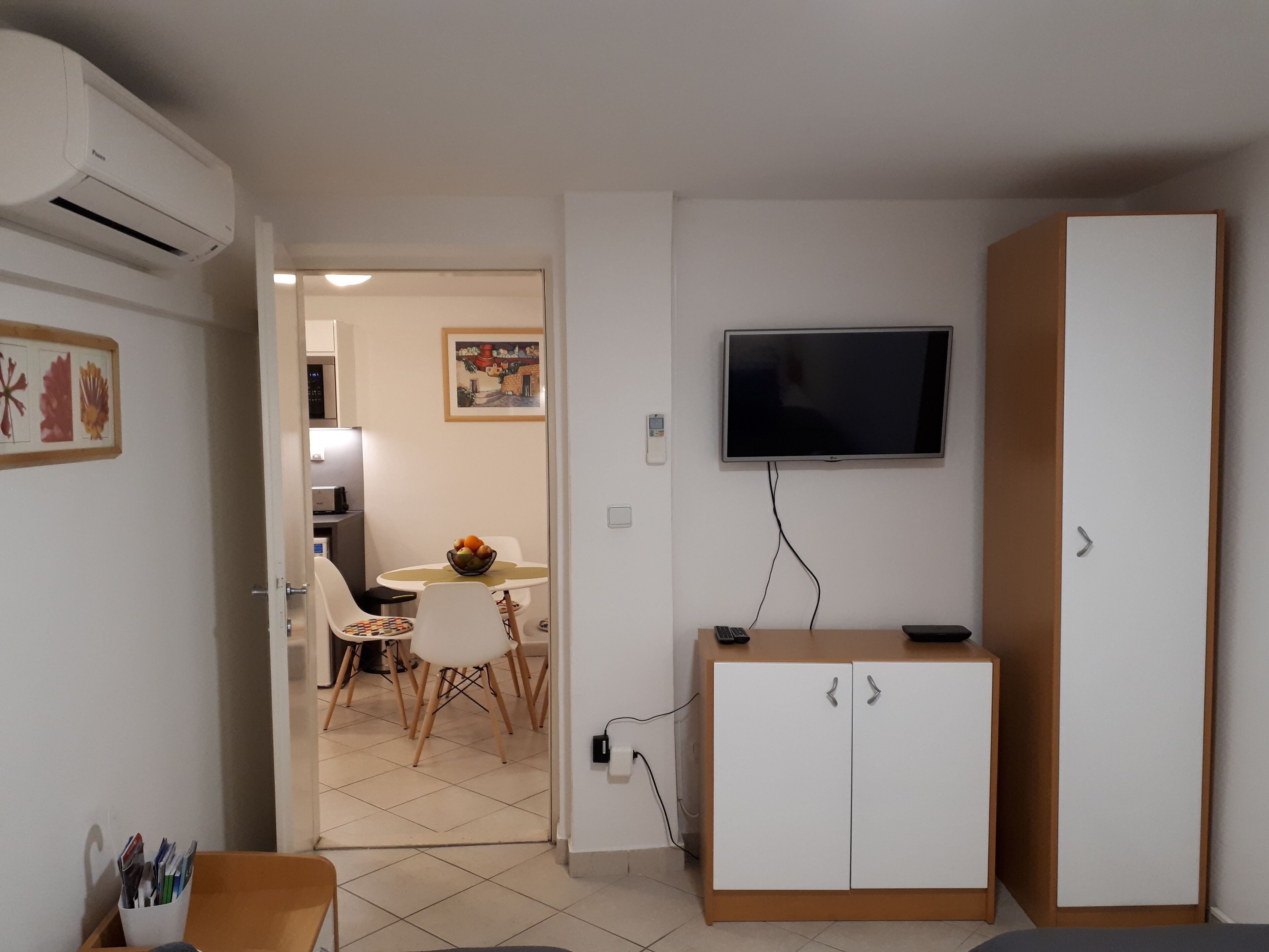 A compact living space with a kitchenette, a dining area, and a TV mounted on the wall.