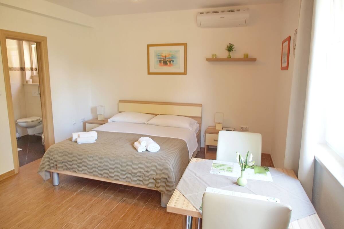 Habitación de hotel con cama, mesitas de noche, escritorio, silla, aire acondicionado y ventana.
