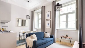 A modern living room with a blue sofa, a dining area, and a kitchen.