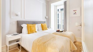 A hotel room with a large bed, a bedside table, a window with curtains, and a framed picture on the wall.