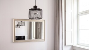 A bathroom with a large mirror, a hanging pendant light, and a window with curtains.