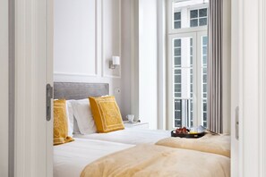 Habitación de hotel con dos camas, una mesita de noche con una taza y una bandeja de fruta, y una ventana con cortinas.