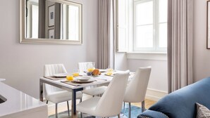 A modern dining area with a white table set for four, a large mirror above, and a view of a window with curtains.