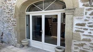 Edifici de pedra amb una porta blanca i panells de vidre, flanquejat per dos planters de pedra.