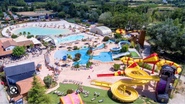 Un complex turístic amb una gran piscina, tobogans aquàtics i una zona de platja.