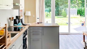 Moderni keittiö, jossa on suuri keittiösaareke, pesuallas ja näkymä puutarhaan liukuovien kautta.