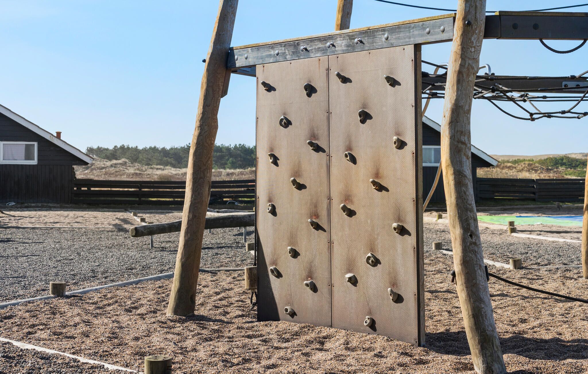 Eine Kletterwand mit vielen Haltepunkten vor einer Holzzahlung und einem Gebäude.
