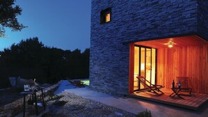 Un edificio moderno de piedra con una terraza de madera y dos sillones de descanso.