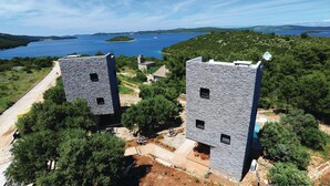 Un edificio de piedra con dos torres, rodeado de follaje y una masa de agua al fondo.