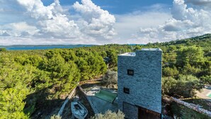 Un edificio moderno con fachada de piedra, rodeado de exuberante vegetación y una vista despejada al mar.