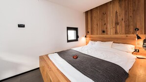 Un dormitorio con cabecera de madera, una ventana pequeña y una lámpara de noche.