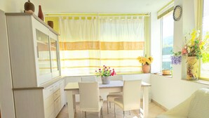 Eine helle Küche mit Esstisch, Stühlen und einem Schrank. Auf dem Fensterbrett stehen Blumen und auf dem Schrank eine Vase.